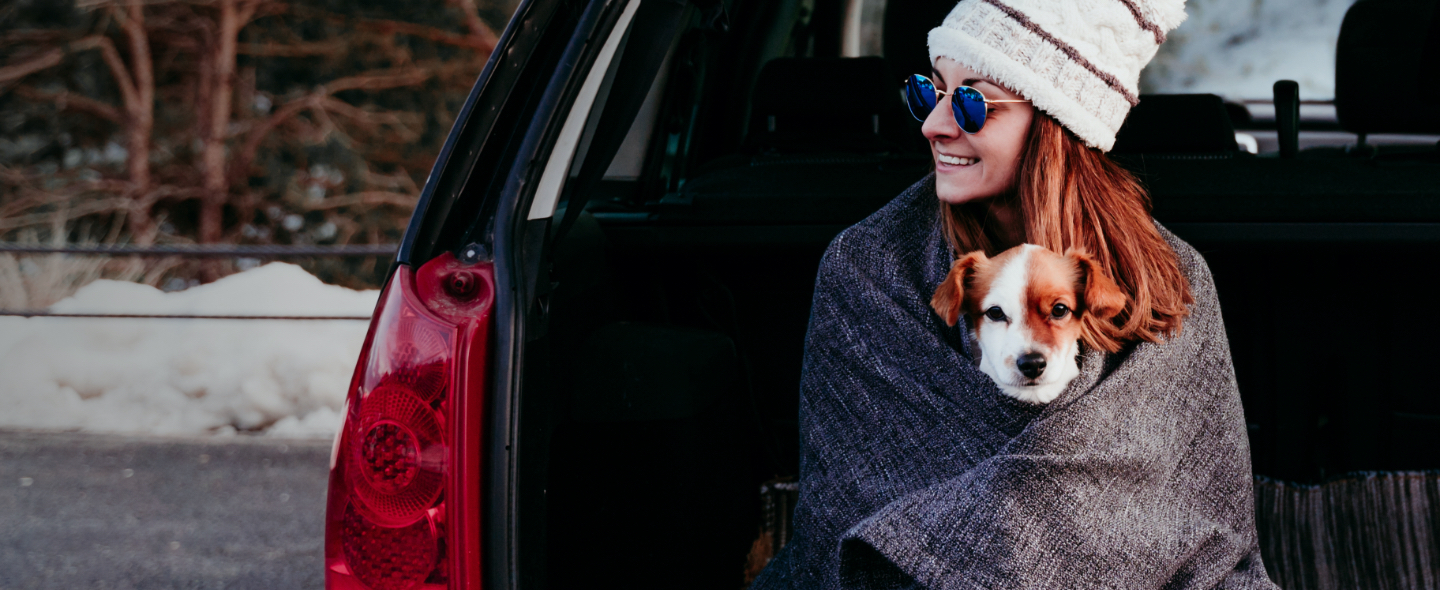 Woman holds dog while sitting on her tailgate.