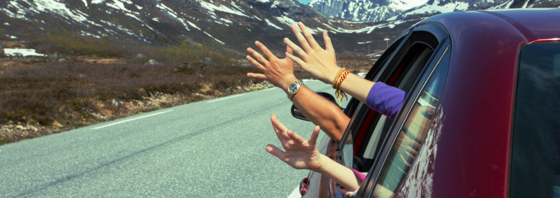 Family waves out a car window while driving among beautiful Alaskan mountains.